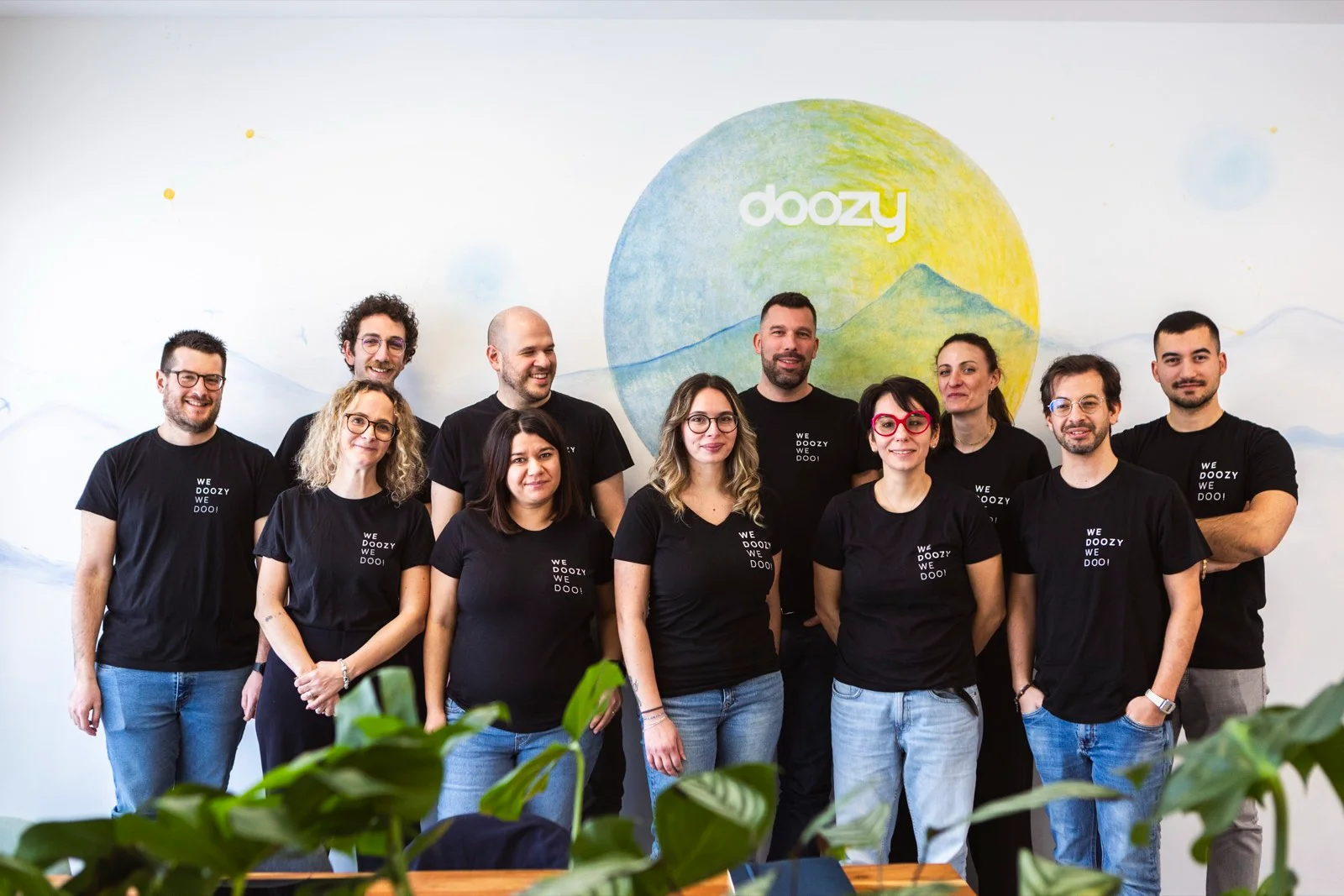 Il team Doozy al completo, undici persone in fila con la t-shirt nera 'We Doozy We Do!', davanti al murales col cerchio Doozy verde e blu nell'ufficio di Selvazzano