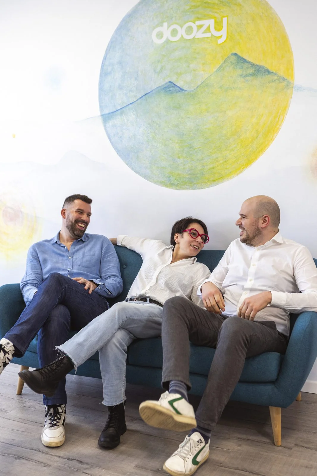 Tre persone del team Doozy in conversazione sul divano dell'ufficio di Selvazzano davanti al murales del logo